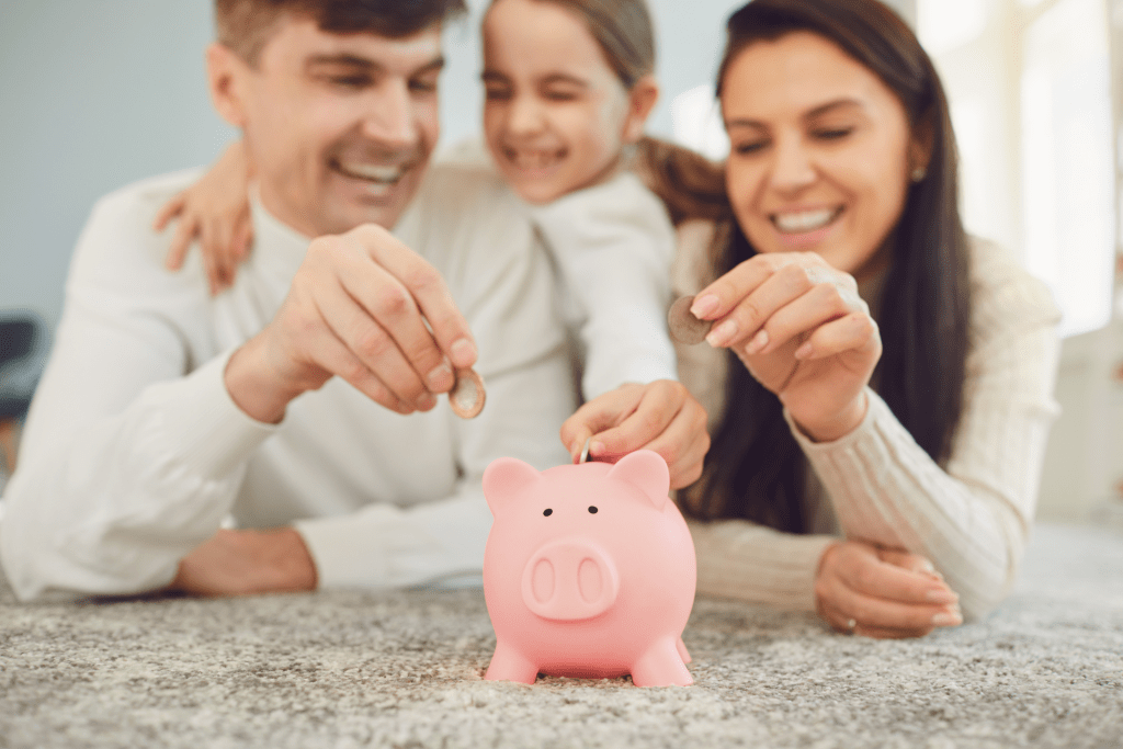 Happy parents and daughter putting coins in a piggy bank showing the importance of teaching financial to kids