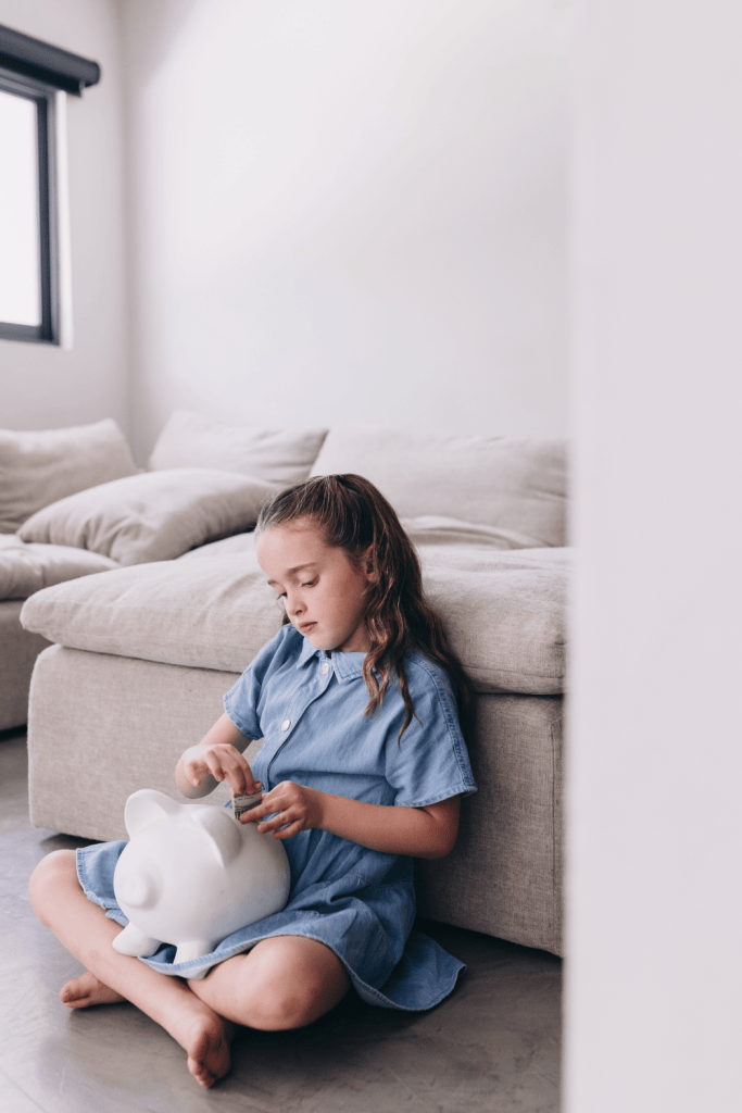 Sad kid sitting on the floor holding her piggy bank representing the Signs of Scarcity mentality in Kids