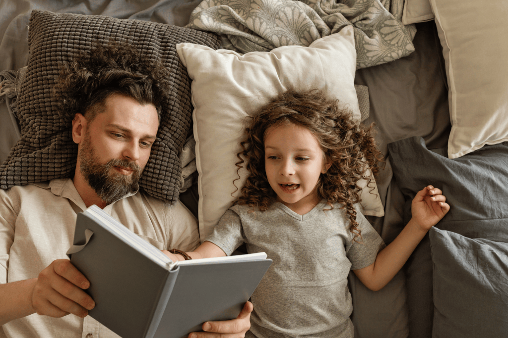 Father and daughter reading in bed showing that Abundance vs Scarcity Mindset can be taught using the right book