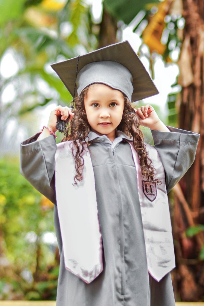 Little girl wearing graduation gown and hat representing that it is important to involve the kids in saving money for college